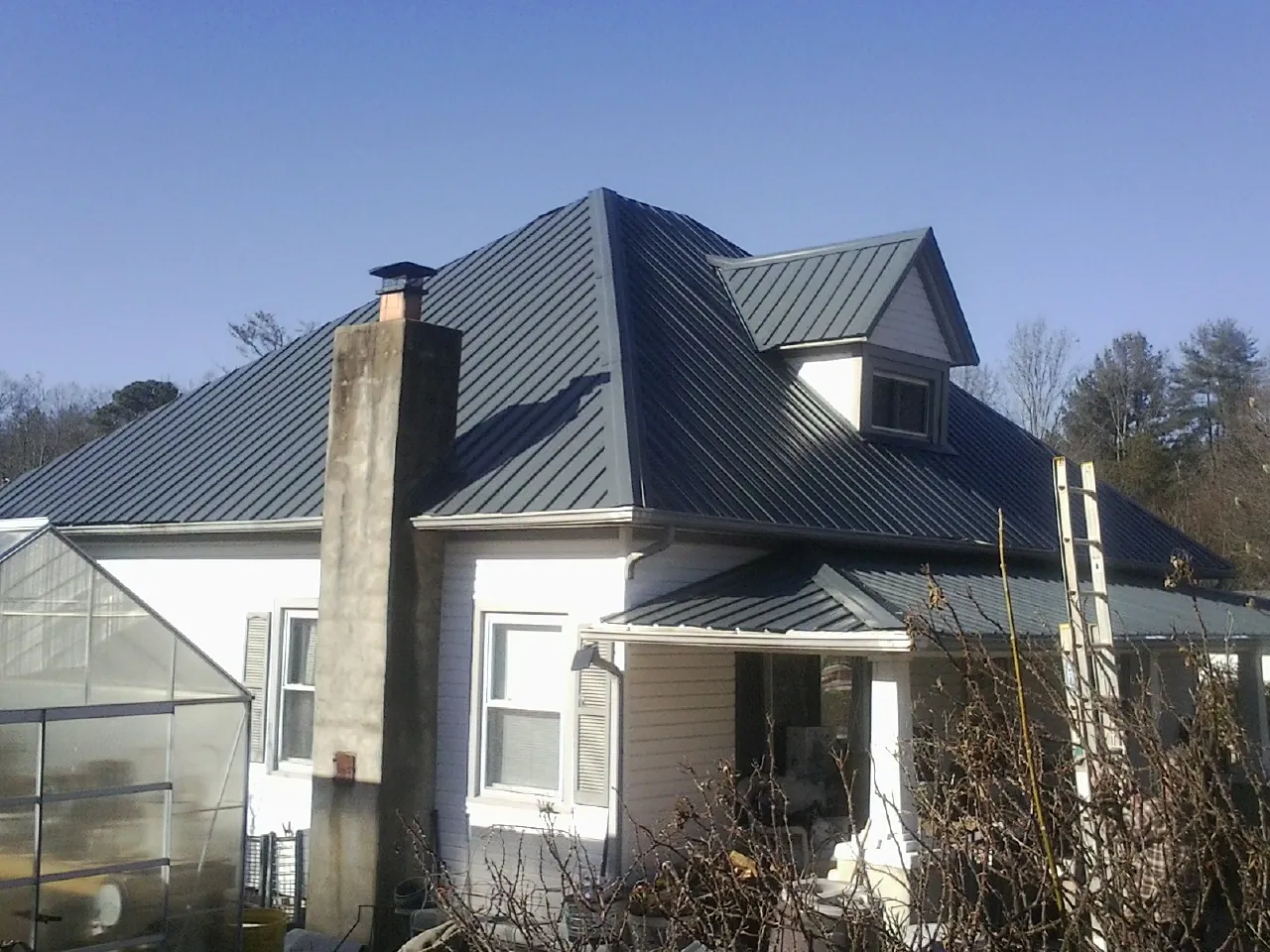 Dark blue standing seam metal roof on a white farmhouse with dormer — Slate & Tile Roof Repair by Roofing Brothers in Fort Branch
