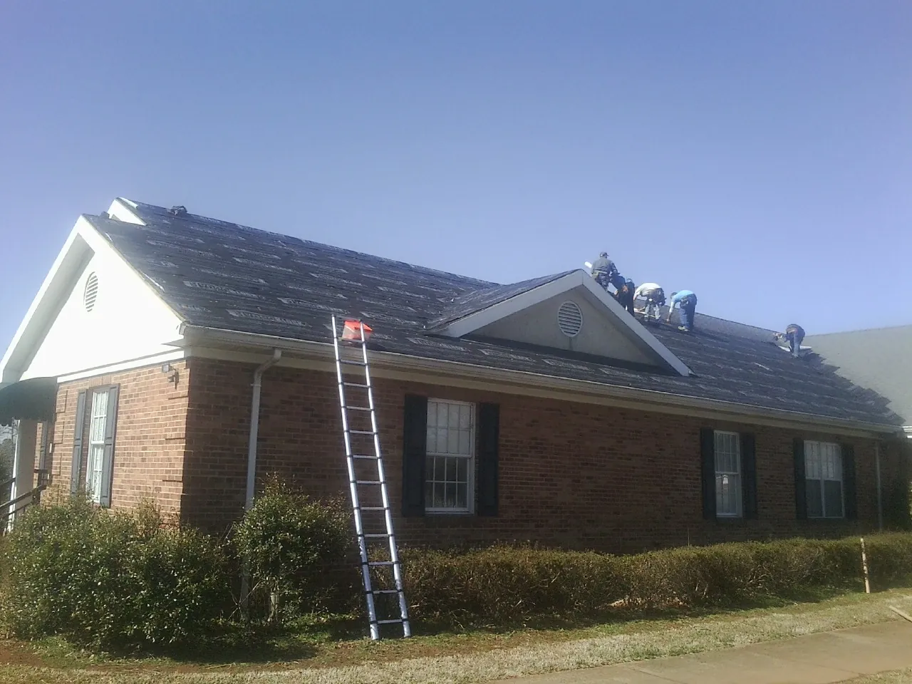 Crew tearing shingles off a brick ranch roof with a ladder set — Emergency Roof Repair work by our crew in Fort Branch