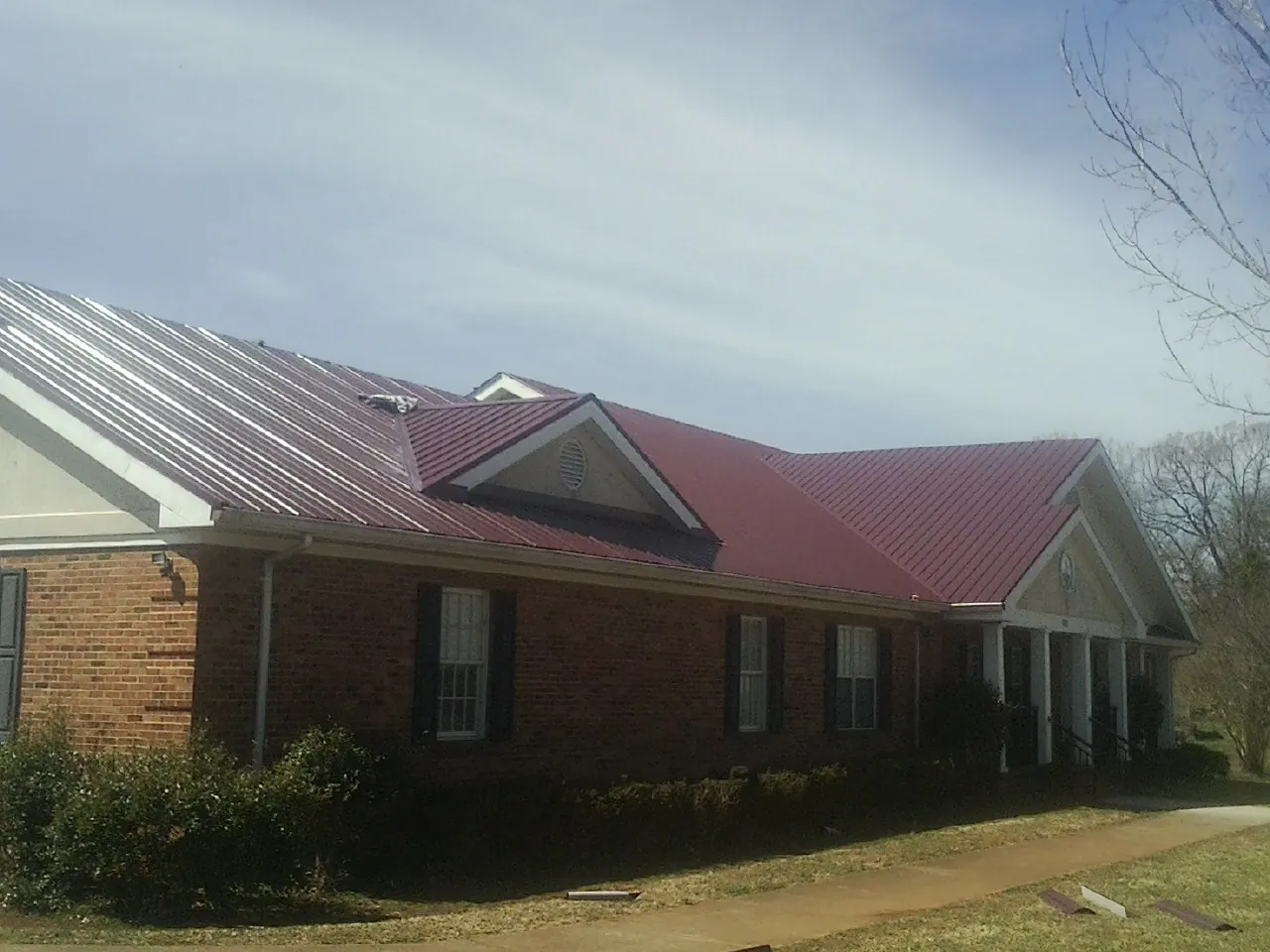 Red metal roof with gabled entries on a long brick building, from a Hail Damage Roof Repair job in Fort Branch