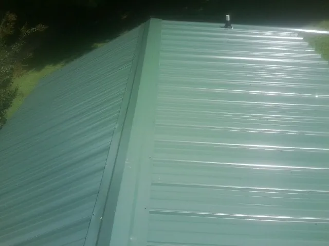 New green metal panels meeting at the ridge of a roof — Flat Roof Repair work by our crew in Fort Branch