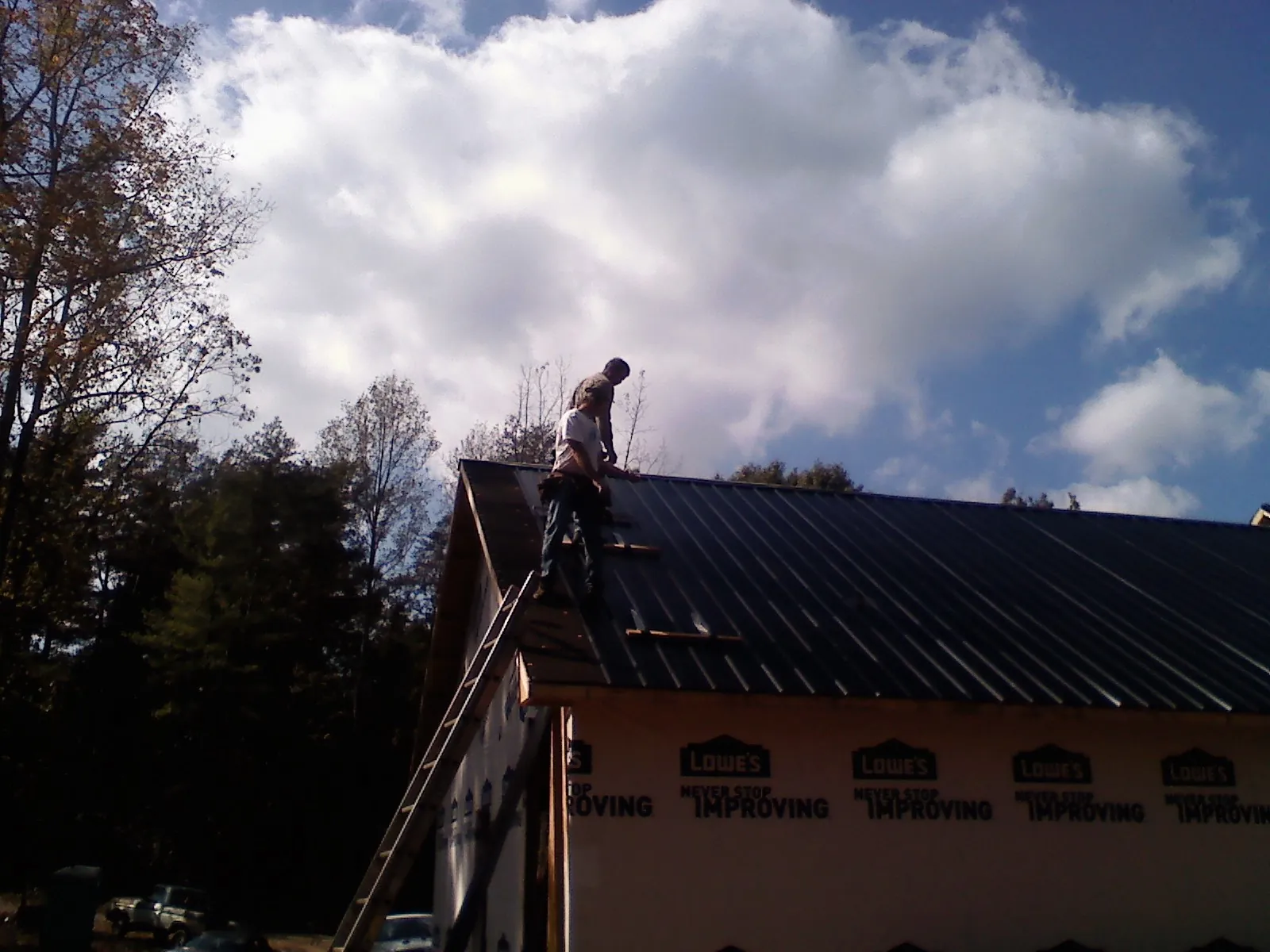 Roofer fastening dark metal panels high against a cloudy sky, from a Roof Inspection job in Fort Branch