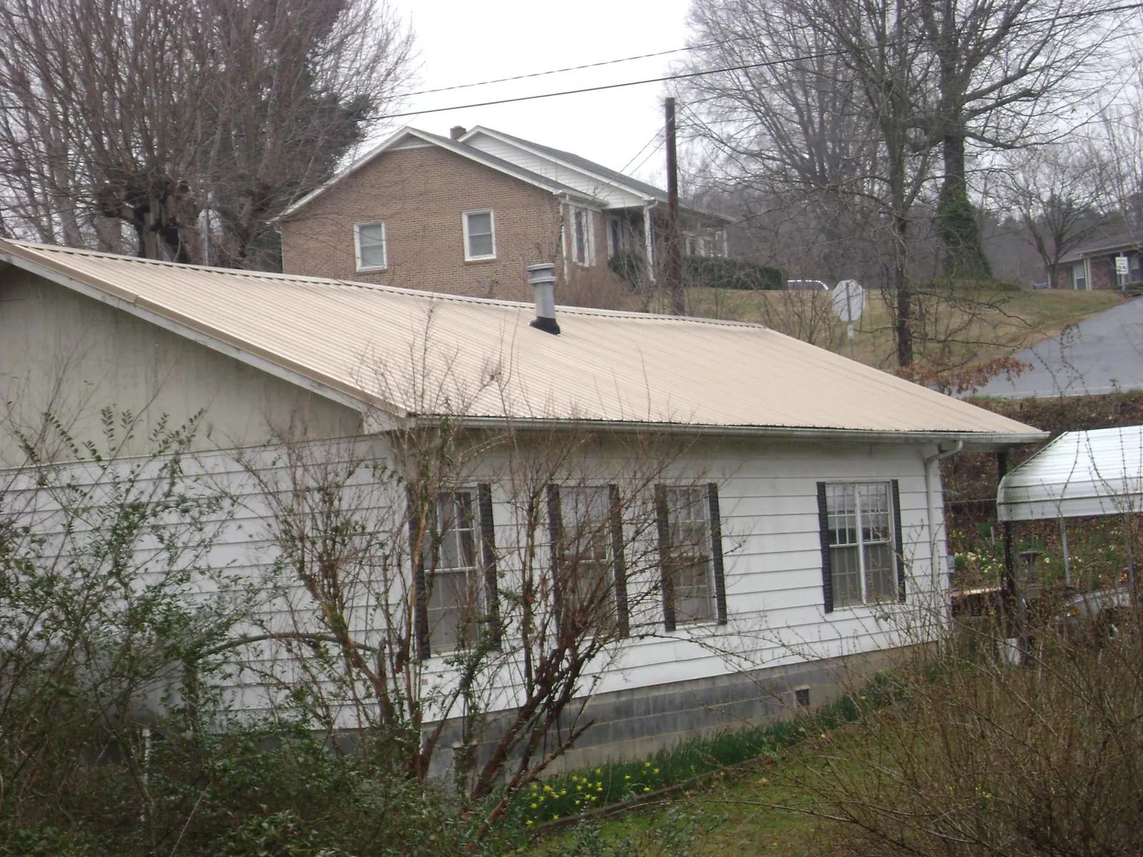 Tan metal roof on a white sided house set into a hillside — Commercial Roofing by Roofing Brothers in Fort Branch